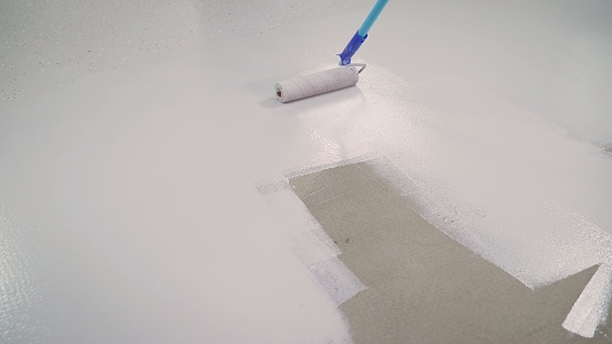 Concrete Floor repair work. Paint roller in construction site. A worker paints the concrete floor with a roller white.