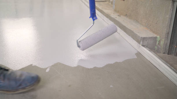 Application of white paint to the concrete floor. Primer for concrete floor before finishing. Repair in the house. Copy space. The master paints the floor with white paint. stock photo