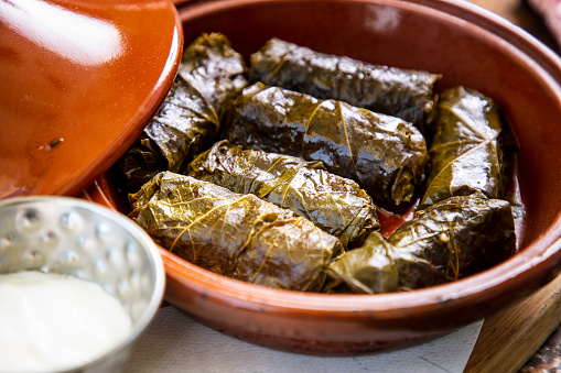 Dolma in green vine leaves served in pottery bowl, sour cream in bowl as dressing, Mediterranean and Middle Eastern cuisine