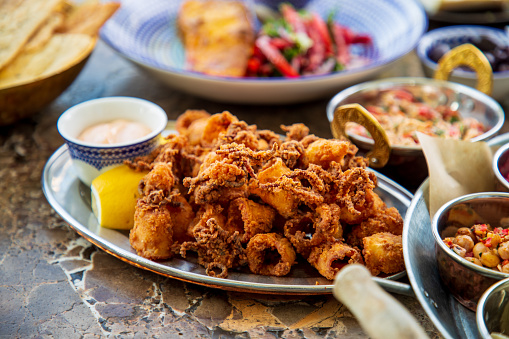 Deep fried calamari rings and tentacles served with lemon and dipping sauce on oval silver plater, Mediterranean specialty on Middle Eastern buffet