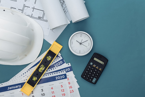 Construction helmet, blueprint and calendar, calculator and clock on blue background. Construction time