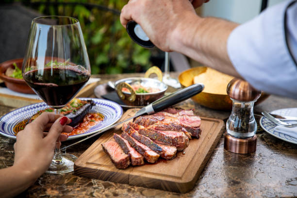 seasoning medium rare steak with salt grinder, cut on wooden board on restaurant table - meat steak veal beef imagens e fotografias de stock