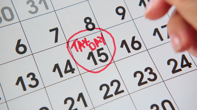 Closeup Womans hand of writing TAX DAY on calendar, April15 or July each year.