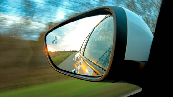 A car passenger view from a car window, looking into the wing mirror as the car drives down a countryside road.