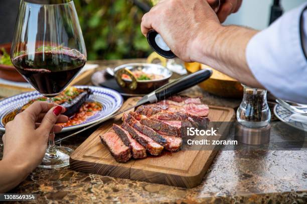 Seasoning Medium Rare Steak With Salt Grinder Cut On Wooden Board On Restaurant Table Stock Photo - Download Image Now