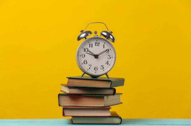 istock Retro alarm clock on a stack of books. Yellow background 1308569713