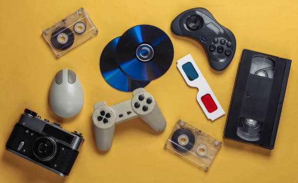 istock Retro entertainment. Attributes, gadgets 80s. Keyboard, pc mouse, compact discs, gamepad, anaglyph glasses, audio and video cassette, camera on yellow background. Top view. Flat lay 1308570024