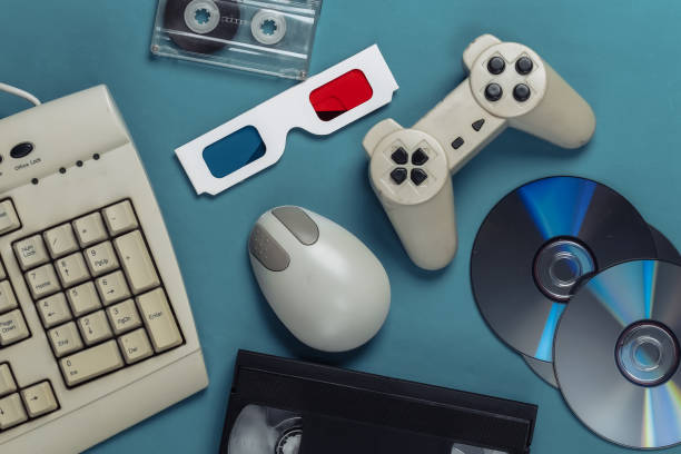istock Retro entertainment. Old-fashioned keyboard, pc mouse, compact discs, gamepad, anaglyph glasses, audio and video cassette on blue background. Top view. Flat lay 1308570039