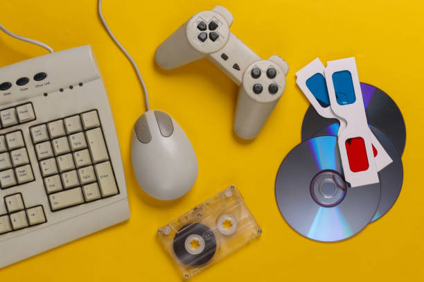 istock Retro entertainment. Old-fashioned keyboard, pc mouse, compact discs, gamepad, anaglyph glasses, audio cassette on yellow background. Top view. Flat lay 1308570052