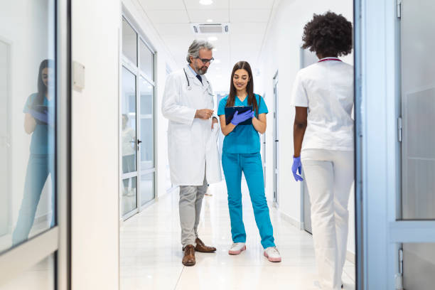 여성 외과 의사와 의사가 병원 복도를 통해 걸어, 그들은 환자의 건강에 대해 이야기하는 동안 디지털 태블릿 컴퓨터를 상담. 전문 직원과 현대 밝은 병원. - computer medical student hospital nurse 뉴스 사진 이미지