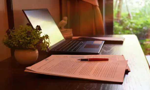 red pen over blurred paperwork on wooden table with laptop