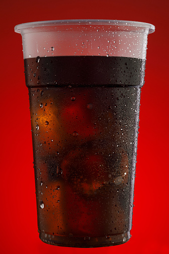 Glass of coca cola drink. Plastic takeaway cup, Drinking glass. Ice Cold Disposable Cup, With Water Drops -Condensation, on red backgrounds