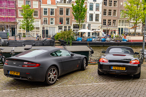 Aston Marint Vangtage en Porsche Boxster parked at a canal in Amsterdam during a springtime day.
