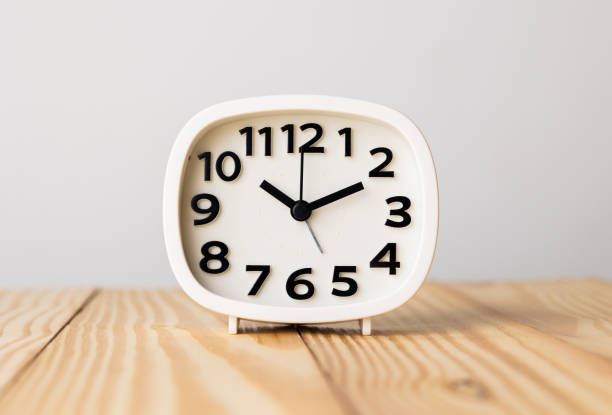 istock Small white alarm clock, black numbers, set the time for 10.10 o'clock, placed on a wood table. 1308586109