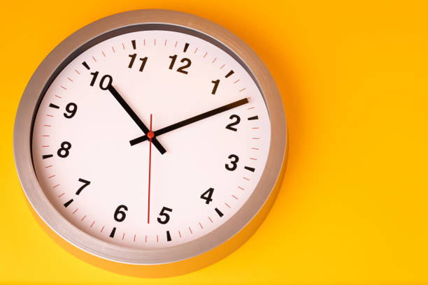 istock Large white alarm clock, black numbers, set the time placed on a table. Clock on isolated yellow background. 1308586144