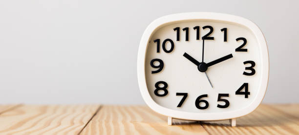 istock Small white alarm clock, black numbers, set the time for 10.10 o'clock, placed on a wood table. 1308586184