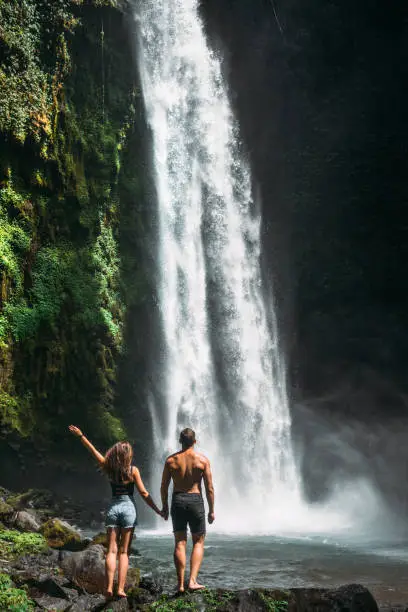 Photo of Couple at the waterfall, rear view. Couple on vacation in Bali. Honeymoon trip. A couple in love travels the world. Vacation on the island of Bali. Tourists in Bali. Copy space