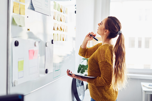 Young businesswoman planning in office using whiteboard and digital tablet