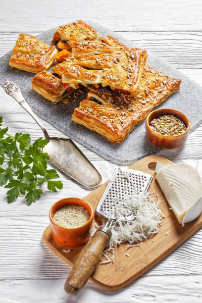 tarte américaine de pâte feuilletée de légumes avec le fromage de chèvre garni de graines de tournesol et de sésame remplies de légumes rôtis servis avec des ingrédients sur une table en bois blanc, vue verticale, plan rapproché - puff pastry pumpkin garlic cheese photos et images de collection