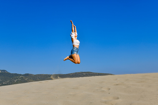 Young woman jumping with happiness on the dunes.
