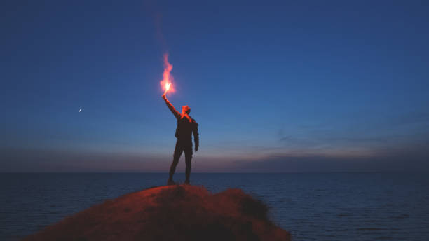 the man with a fire stick standing on the mountain top near the sea - climbing men sea cliff imagens e fotografias de stock