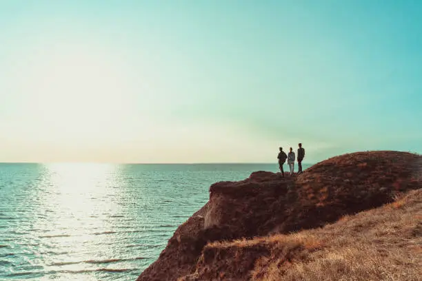 Photo of The three people standing on the mountain top near the sea