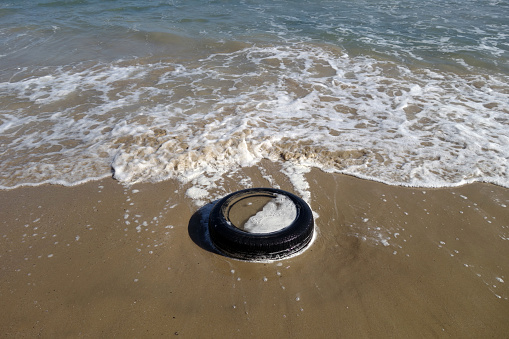 Used car tyre on the sea beach. Ecological and environment isues.