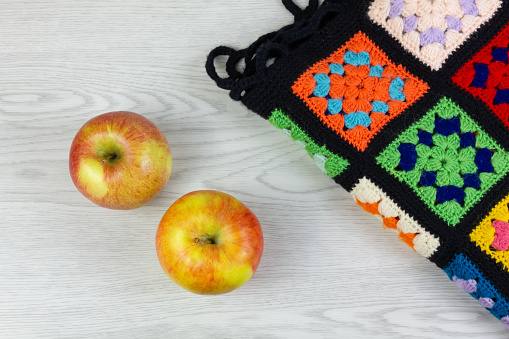 Above view of two yellow and red apples and a multicolor plaid blanket on a white wooden table