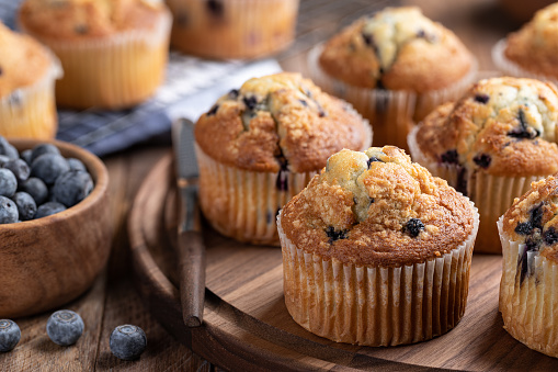 Blueberry muffins on a wooden platter with berries and muffins in background