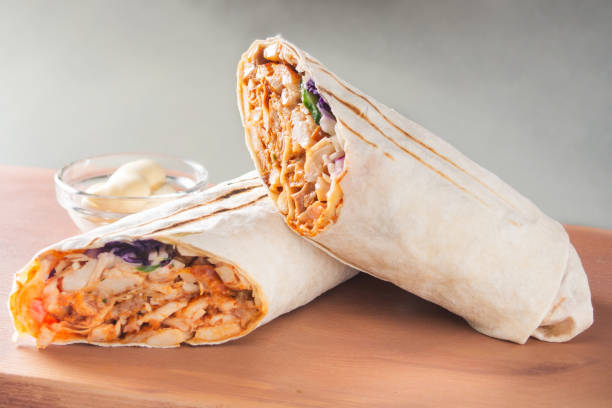 Shawarma sandwich. Lavash roll with chicken, cabbage, cucumber, herbs and sauce on a wooden board. stock photo