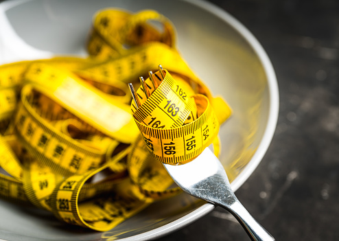 yellow sewing measuring tape wound onto a fork on a white isolated background. weight loss and diet concept