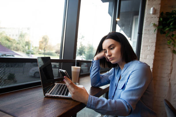 istock Tired female freelancer working in cafe. Concentration problems concept. Upset young woman looking in smartphone and waiting for a call. Cozy coffee shop atmosphere. Cafe or restaurant on background. 1308612041