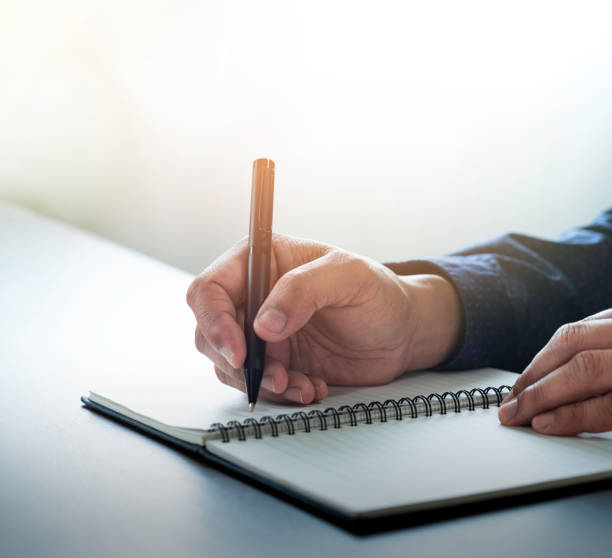 istock Close-up of man hand using writing pen memo on notebook paper or letter, diary on table desk office. Workplace for student, writer with copy space. business working and learning education concept. 1308616825