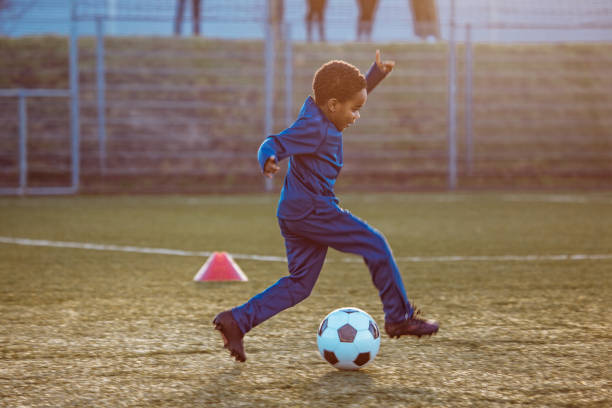 A young black boy child at a soccer training football pitch on a beautiful sunny day in the Netherlands