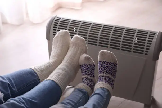 Photo of Mother and child warming feet near electric heater at home, closeup