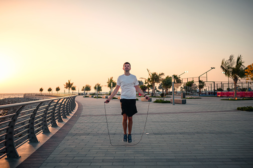 Man doing a jumping rope exercise in a public park by the seaside at sunset during an outdoors workout for staying healthy and fit