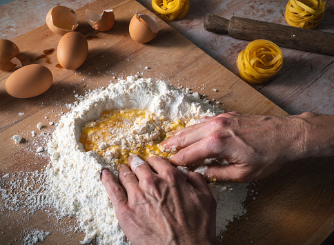 Handmade pasta dough male hands mixing eggs and flour homemade with ingredients and rolling pin
