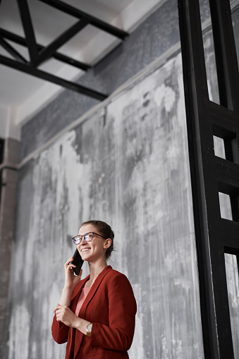 Vertical portrait of successful businesswoman wearing red and speaking by smartphone, copy space