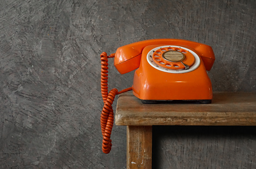 Orange vintage telephone on wooden table background And with cement on the background An old-fashioned representation of communication technology.\