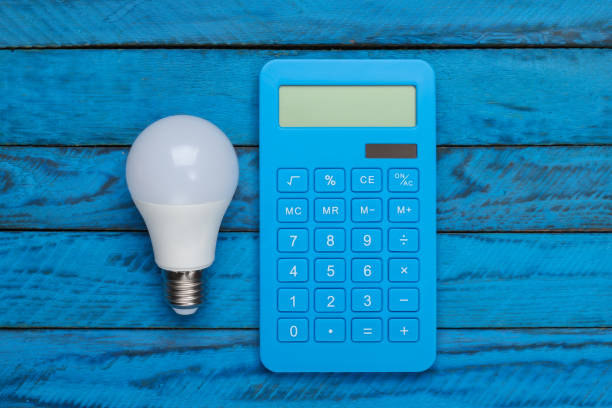 istock Saving electricity. Led light bulb and calculator on blue wooden background. Top view 1308627845