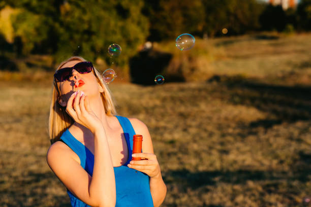 Young Caucasian beautiful woman blowing bubbles in a public park.