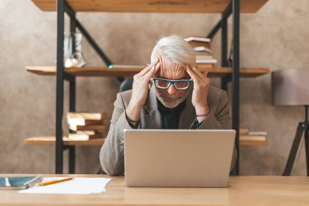 istock Burnout of people. Senior man holding his head at the workplace. Stress and problems at work, overwork. Irritating migraine 1308629894