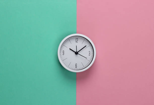 istock White clock on pink blue pastel background. Minimalistic studio shot. Top view 1308630144