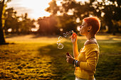 Short hair woman blowing bubbles in a park