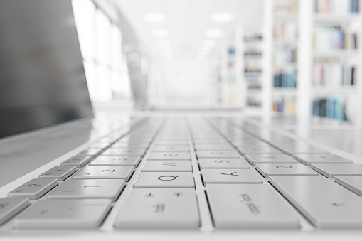 Focus On The Laptop Keyboard With Blurred Library Background.