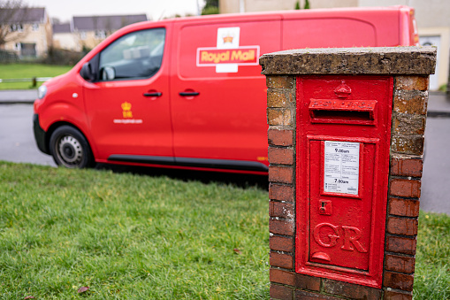 Red vintage mailbox for letters and Royal Mail van, British postal service and courier company