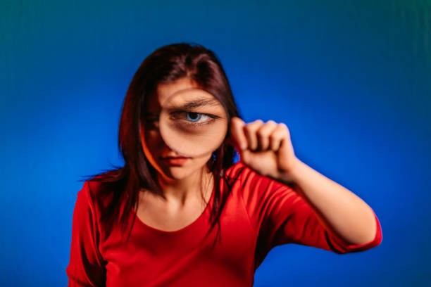 Young pretty serious curious woman looking through magnifying glass.