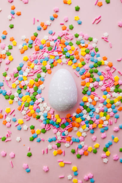 istock White Easter egg on pink background with colourful sprinkles. Yellow, orange, pink, white, blue and green sugar edible decoration  with Easter egg. 1308637120
