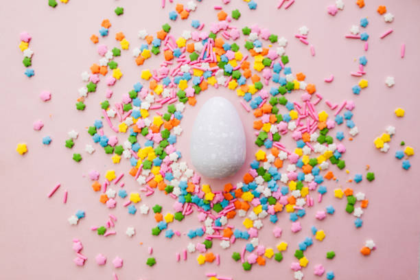 istock White Easter egg on pink background with colourful sprinkles. Yellow, orange, pink, white, blue and green sugar edible decoration  with Easter egg. 1308637137
