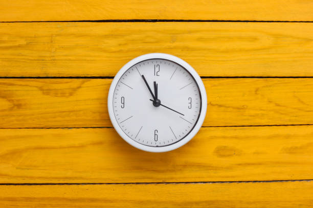 istock White clock on yellow wooden background. Time running away. Top view 1308637182